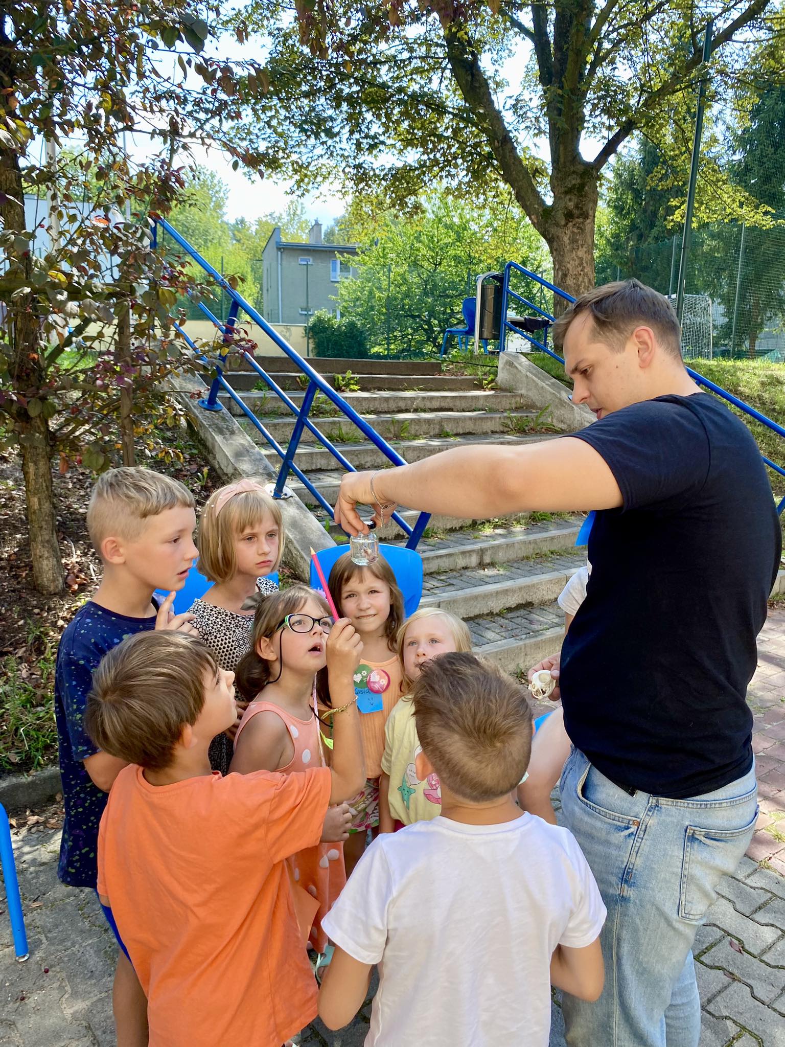 Jeden z organizatorów ŚFN on Tour pokazuje dzieciom szklany pojemnik wypełniony wodą, a w nim okaz zwierzęcia