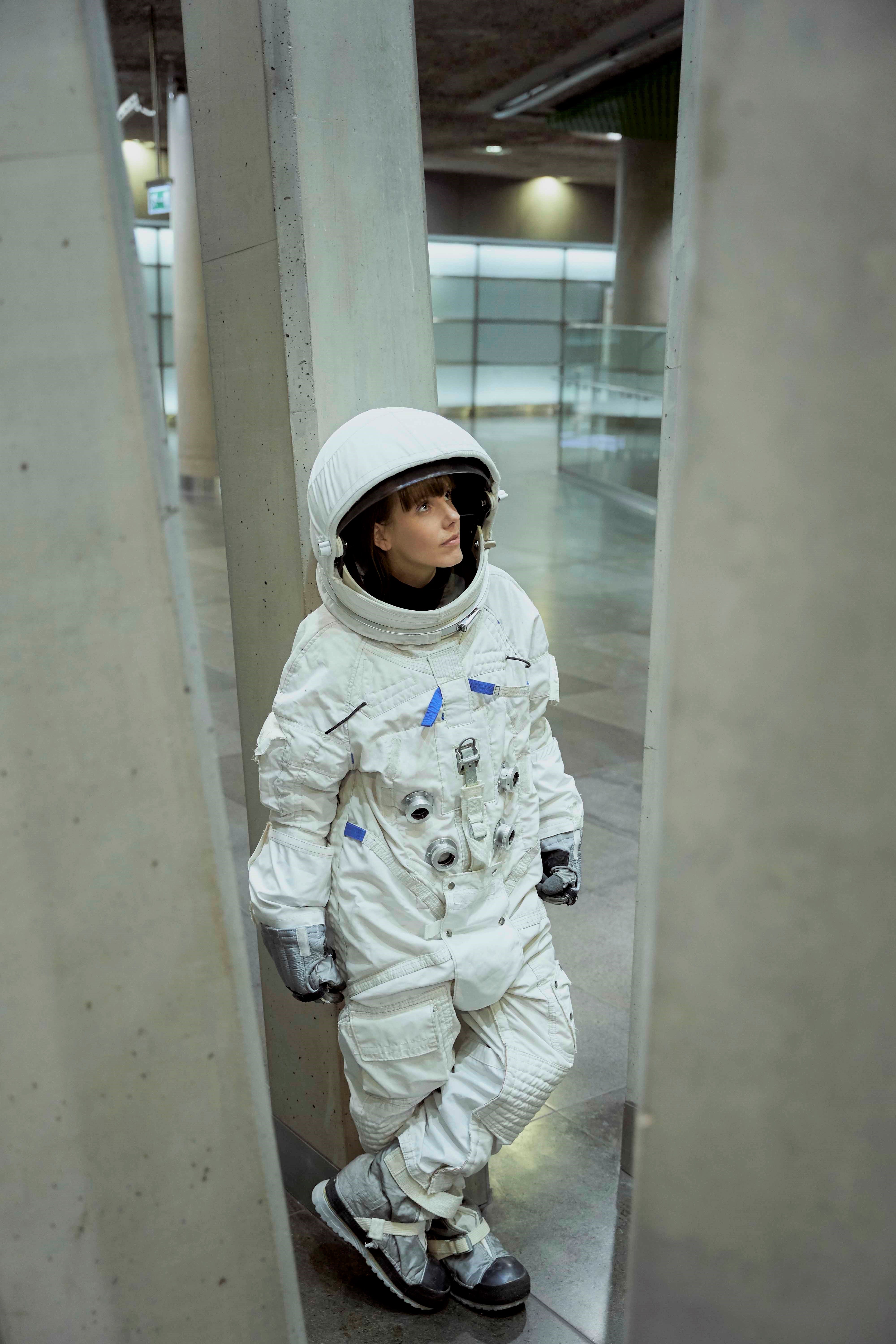 Bohaterka wywiadu ubrana w biały skafander astronauki wśród betonowych szarych kolumn.